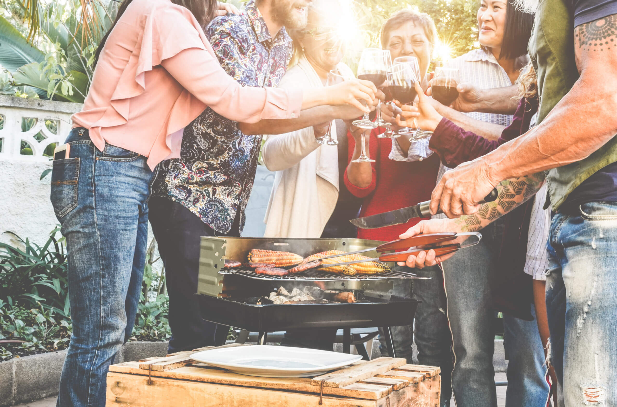 Friends grilling meat and cheering and cooking at bbq meal outdoor - Different age of people having fun at barbecue dinner - Summer lifestyle, friendship and fun concept - Focus on close-up chef hand