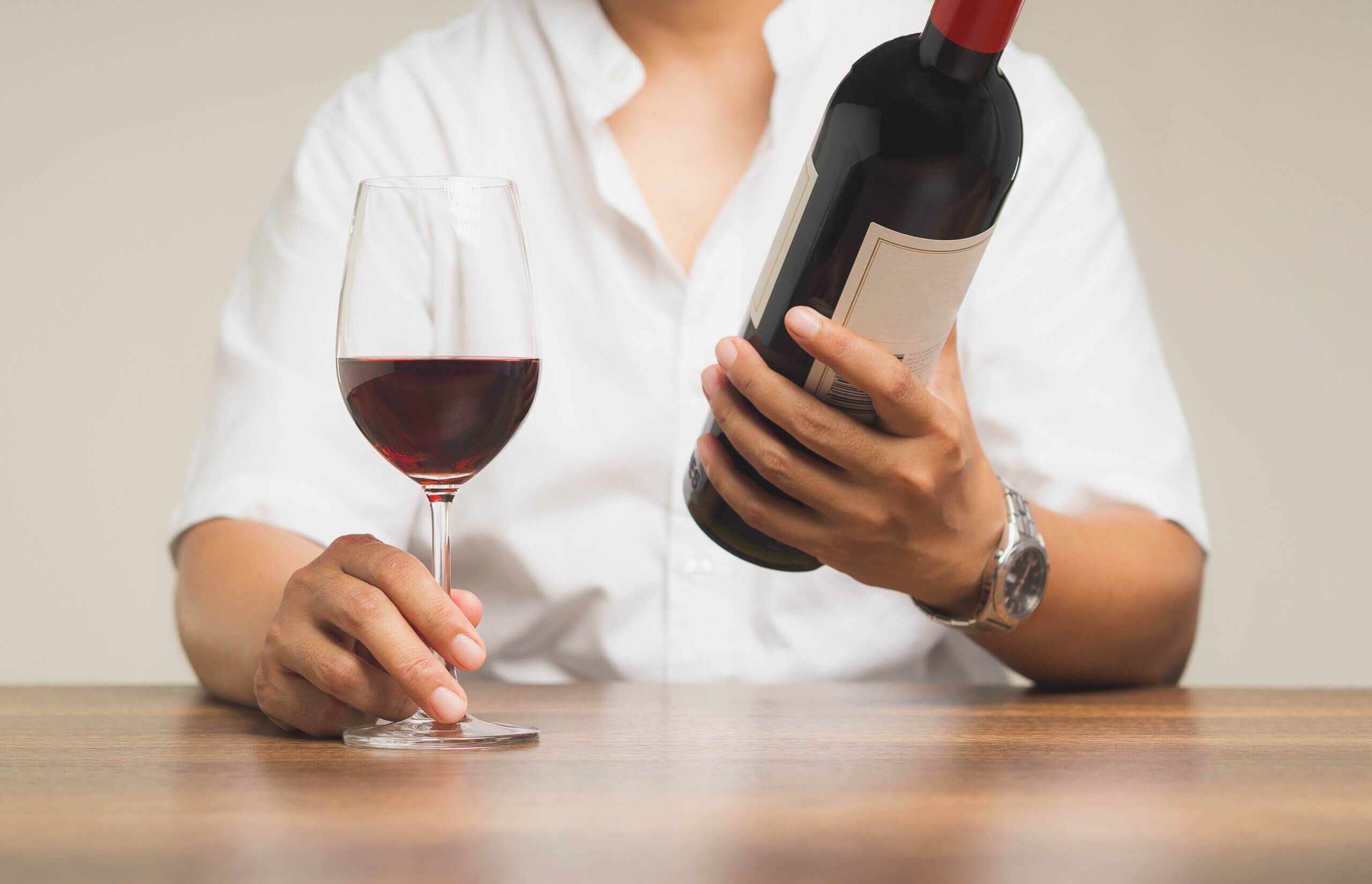 Businessman touches the base of a glass of red wine and holds a wine bottle while sitting at the table. Moment of relaxation. Work-Life balance.