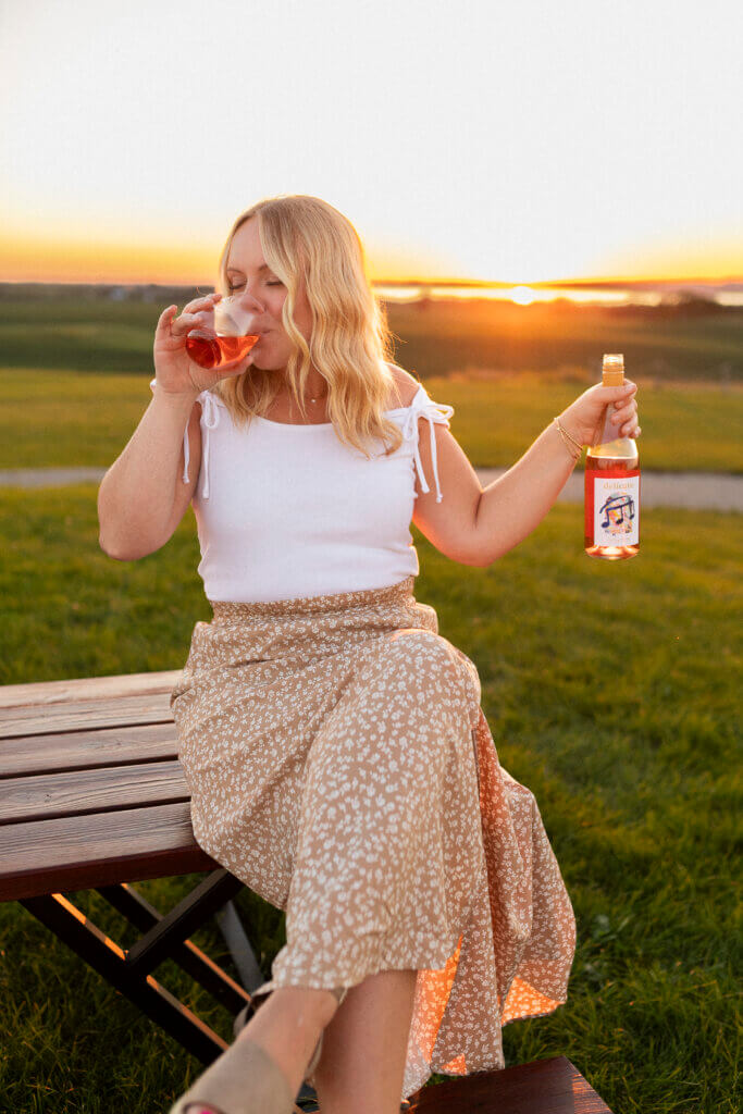 Woman drinking Rolling Forks Vineyard's Delicato Rose' wine while enjoying a sunset over Lake Minnewaska, Glenwood, Minnesota
