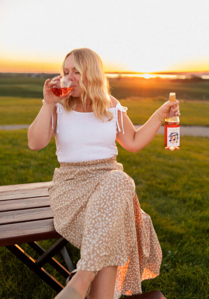 Woman drinking Rolling Forks Vineyard's Delicato Rose' wine while enjoying a sunset over Lake Minnewaska, Glenwood, Minnesota