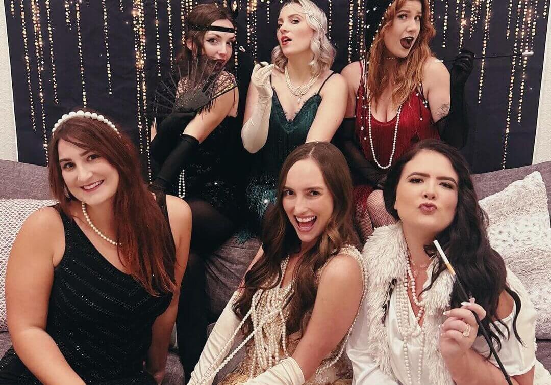 A group of women dressed in 1920s flapper dresses and pearl necklaces laughing together at Rolling Forks Vineyards for a Galentine’s Day celebration.